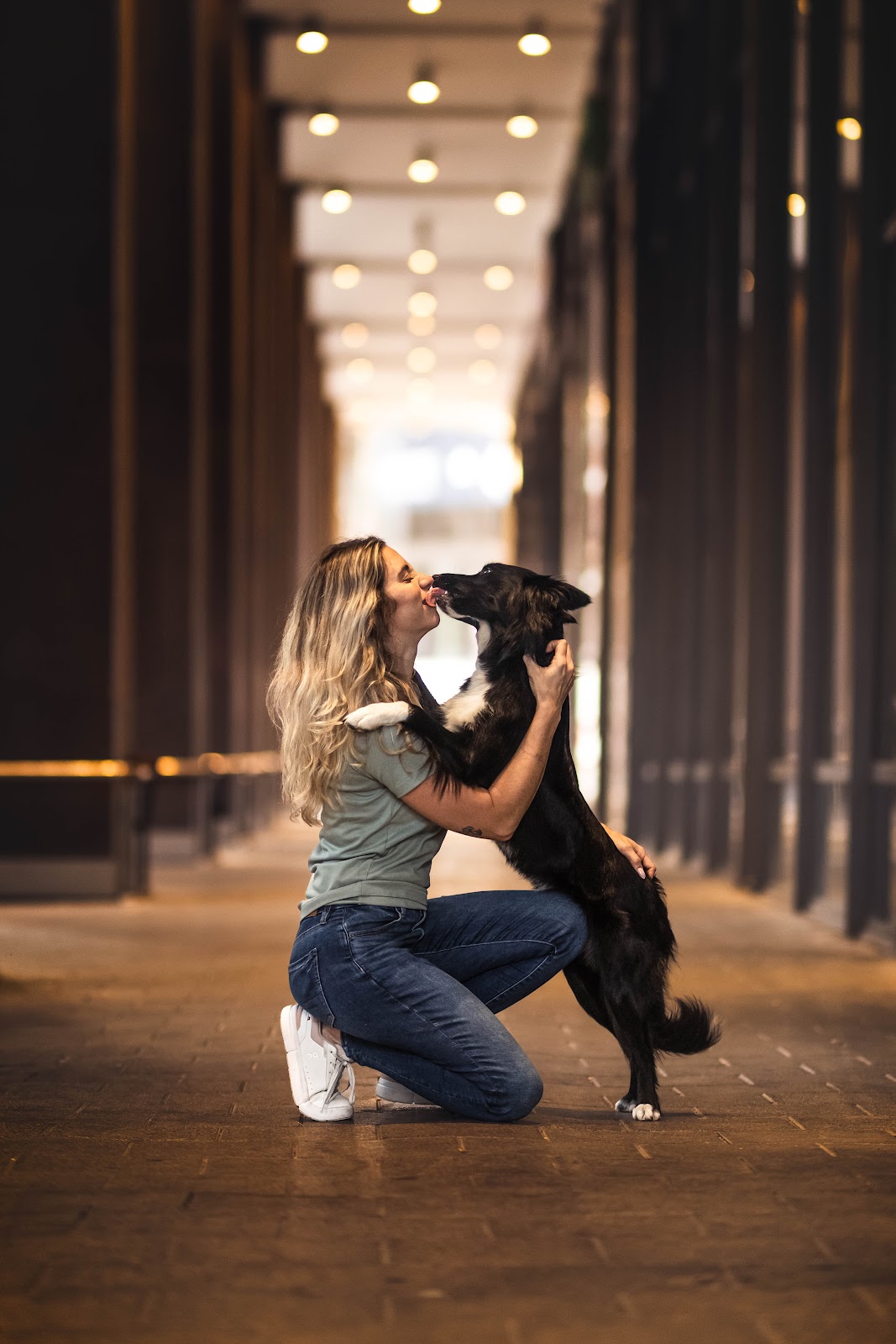 Roni kneeling while her border collie licks her cheek